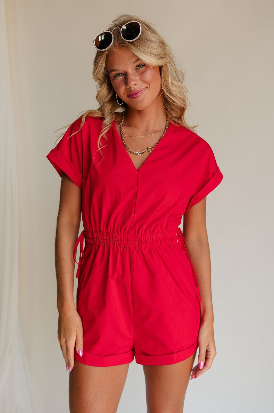 front view of female model wearing the Margot Tie Waist Short Sleeve Romper which features Elastic Waistband with Ties, Lightweight Fabric, V Neckline, Short Sleeves and Side Pockets. the romper is available in red and blue.
