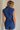 back view of female model wearing the Lila Navy Denim Button-Up Romper which features Navy Blue Washed Fabric, Two Front Pockets, Two Back Pockets, Front Zipper with Button Up Closure, Collared Neckline and Sleeveless