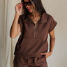 front view of female model wearing the Thea Brown Ribbed Sleeveless Top which features Brown Ribbed Fabric, One Large Front Pocket, Quarter Zip Up, High Neckline, Gold Zipper Side Details and Sleeveless