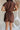 back view of female model wearing the Thea Brown Ribbed Shorts which features Brown Ribbed Fabric, Two Side Pockets, Elastic Waistband with Drawstring Tie and Gold Hardware Details