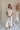Full body front view of female model wearing the Elysia Short Sleeve Ruffle Top that has cream fabric, ruffle details, front pleating, and slit sleeves with ties.