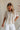 Upper body front view of female model wearing the Elysia Short Sleeve Ruffle Top that has cream fabric, ruffle details, front pleating, and slit sleeves with ties.