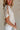 Close side view of female model wearing the Elysia Short Sleeve Ruffle Top that has cream fabric, ruffle details, front pleating, and slit sleeves with ties.