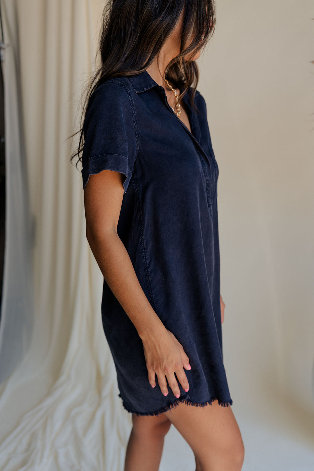 side view of female model wearing the Leighton Navy Fray Short Sleeve Mini Dress which featuresNavy Blue Tencel Fabric, Fray Hem Details, Mini Length, Quarter Button-Up Closure, Collared Neckline, Short Sleeves and Left Front Chest Pocket