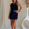 Full body front view of female model wearing the Elara Navy Blue Shorts that have navy blue fabric and a back zipper. Worn with matching tank top.
