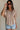 Upper body front view of female model wearing the Elysia Short Sleeve Ruffle Top in Taupe that has taupe fabric, ruffle details, front pleating, and slit sleeves with ties.