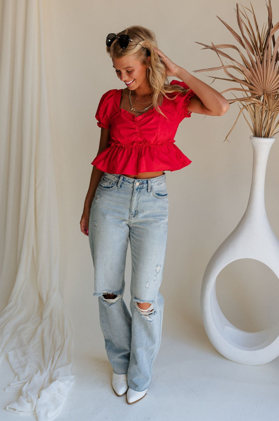 Full body front view of female model wearing the Monet Red Puff Sleeve Crop Top that has red fabric, puff short sleeves, a cropped flared waist, and an open back with a tie.