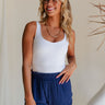 Upper body front view of female model wearing the Quinn White Sleeveless Bodysuit that has white knit fabric and a thong bottom. Worn with navy shorts.