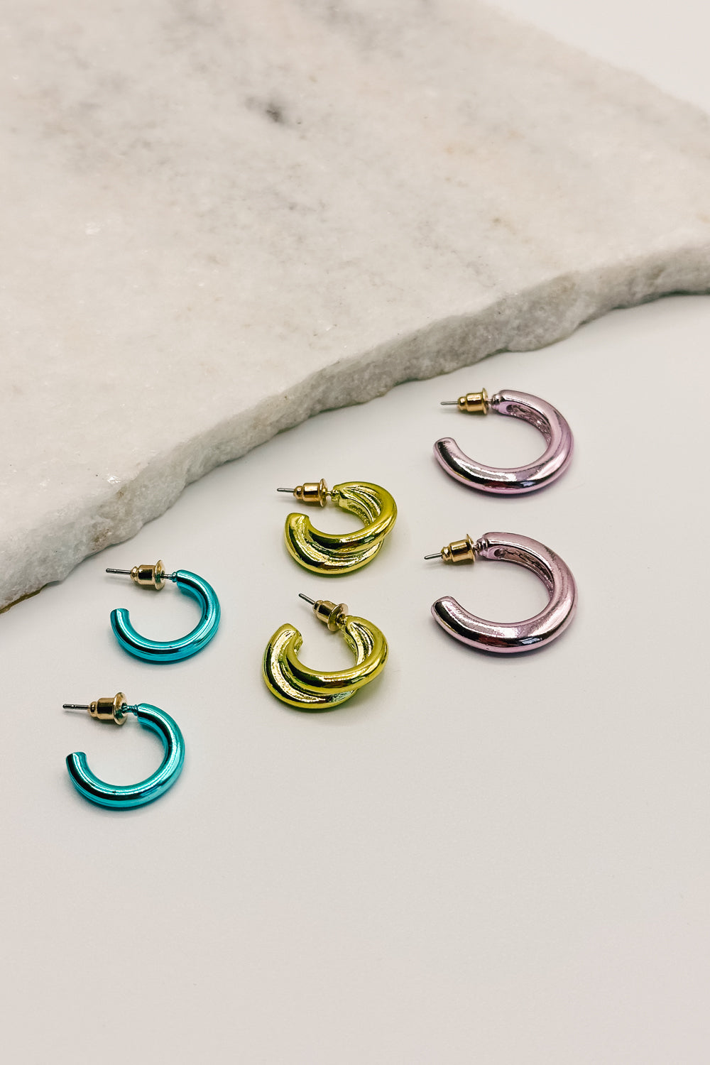 close up view of the Remi Multi Mini Hoops Earring Set which features small teal, lime green and medium size lavender open hoops