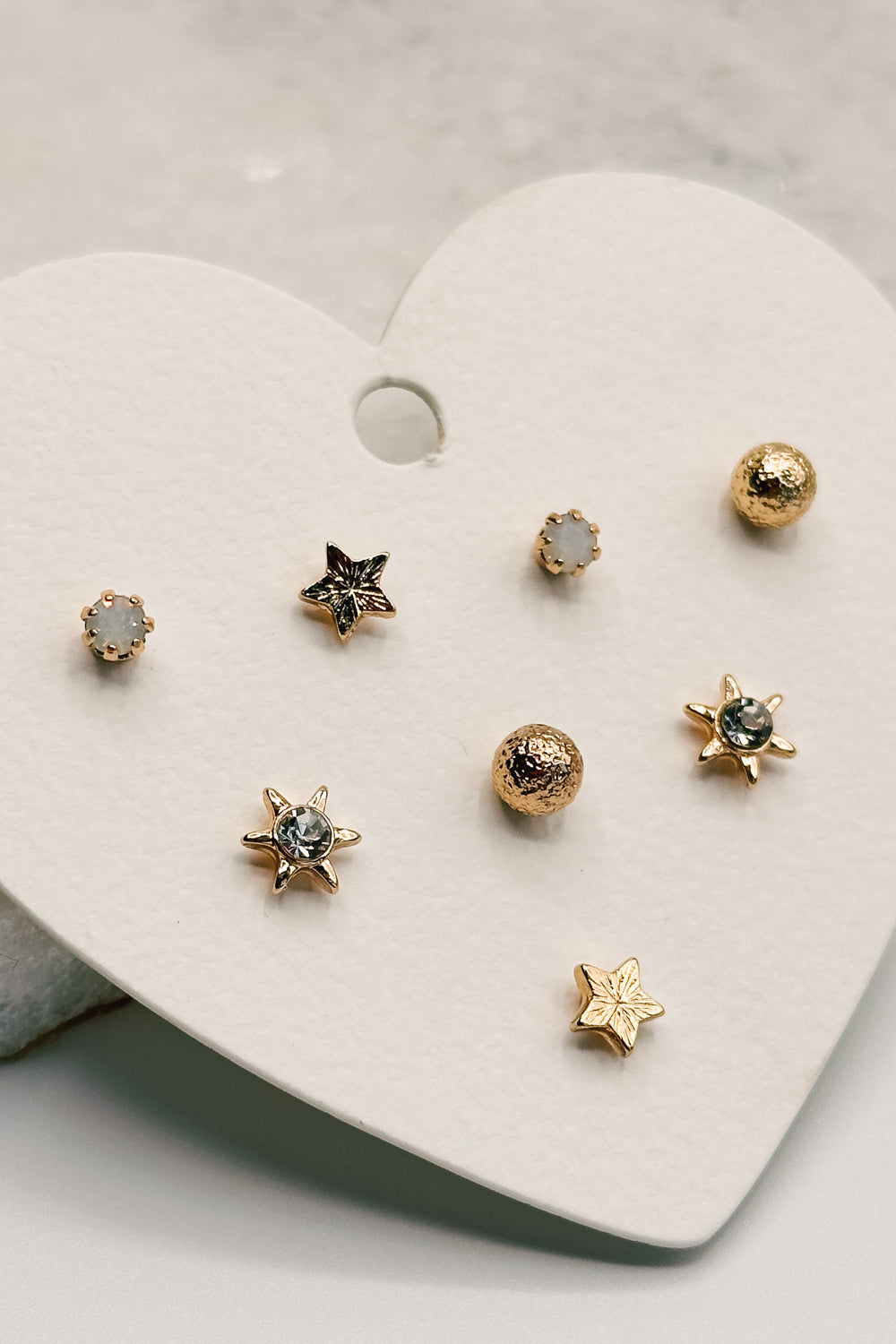 close up view of the Lucia Gold Starburst Stud Earring Set which features set of stud earrings include stars, starburst, clear studs and gold beads