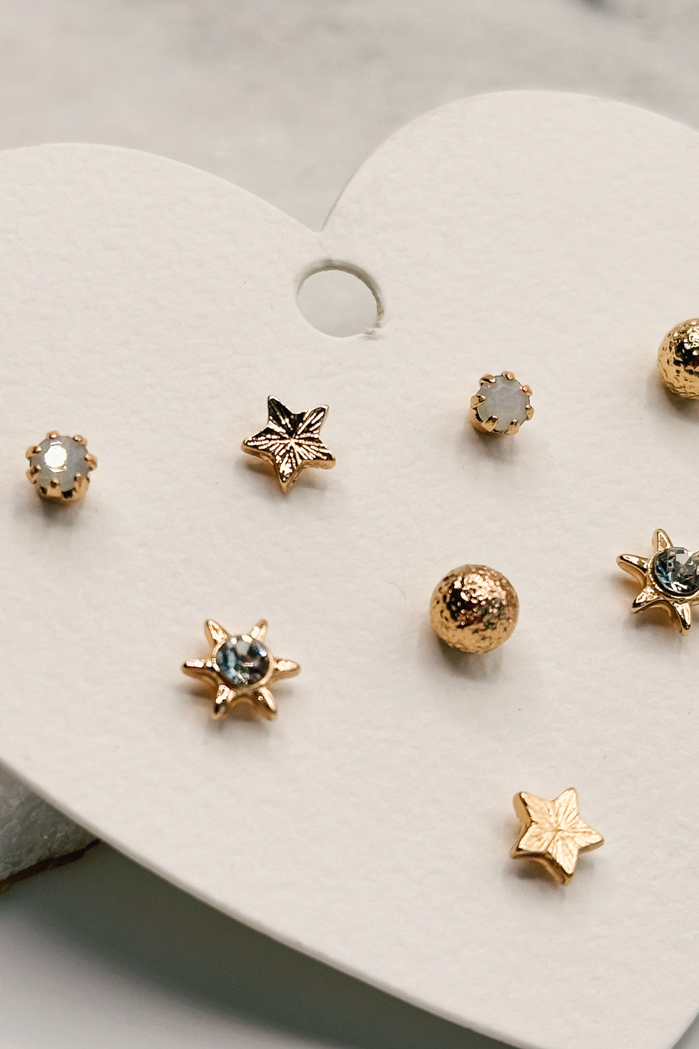 close up view of the Lucia Gold Starburst Stud Earring Set which features set of stud earrings include stars, starburst, clear studs and gold beads