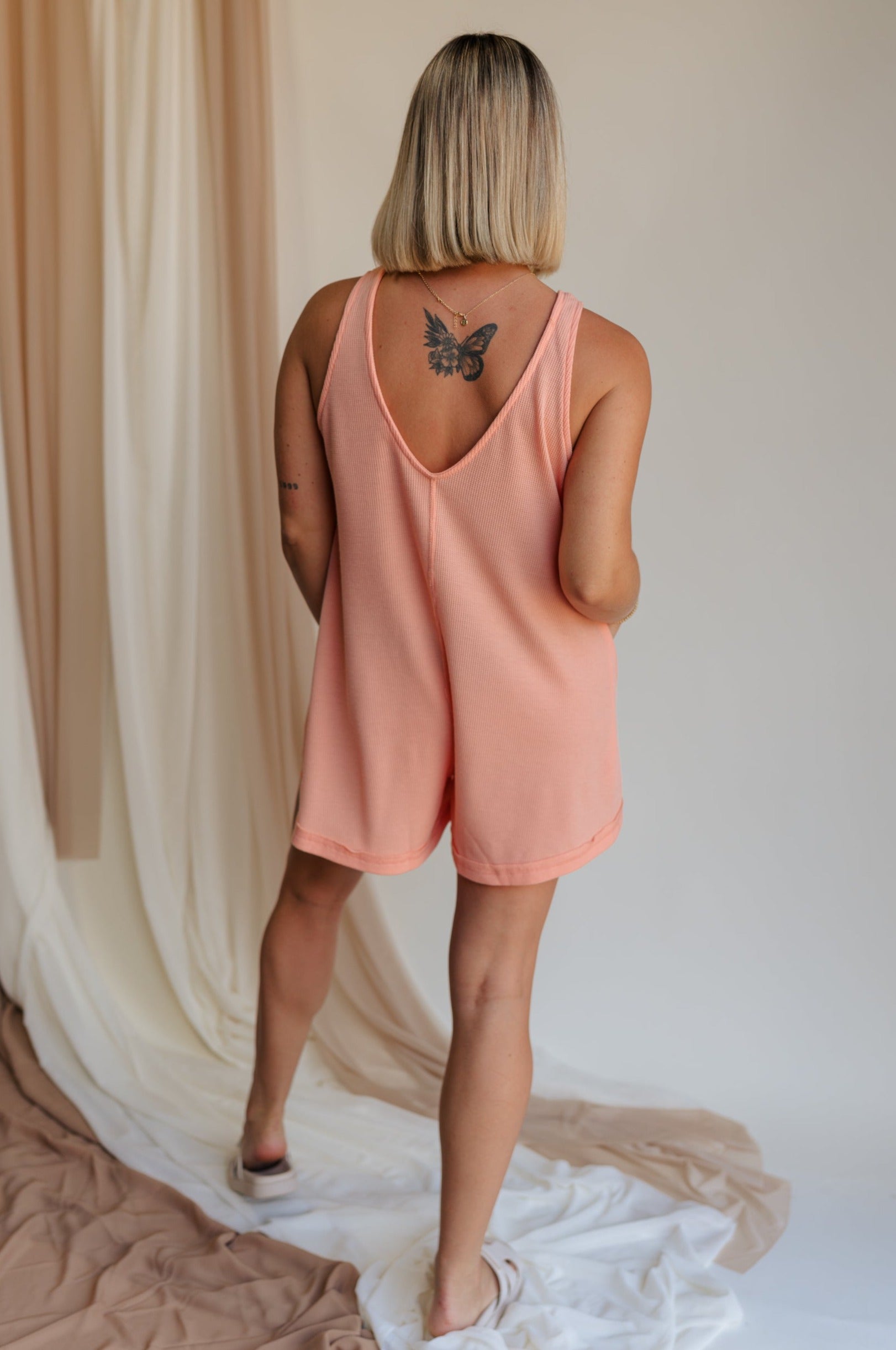 Back view of model wearing Mckenna Coral Romper. This is a coral textured sleeveless romper with ribbed material.