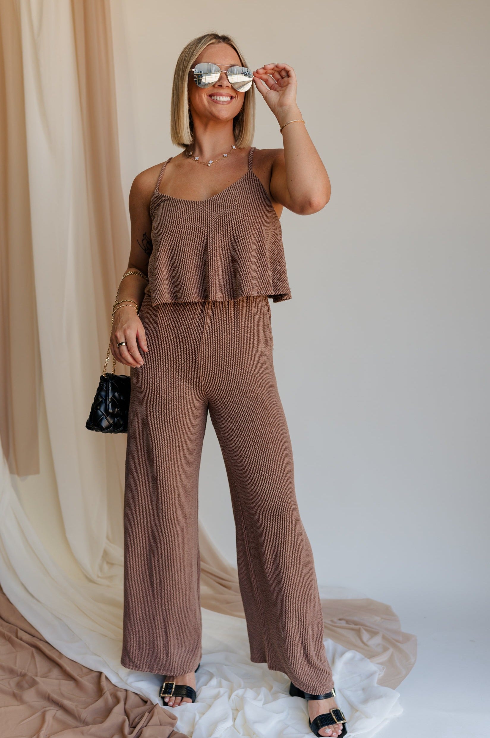 Full body view of model wearing Kaylee Brown Ribbed Jumpsuit. This is a brown ribbed jumpsuit, with ruffle upper, and adjustable straps.