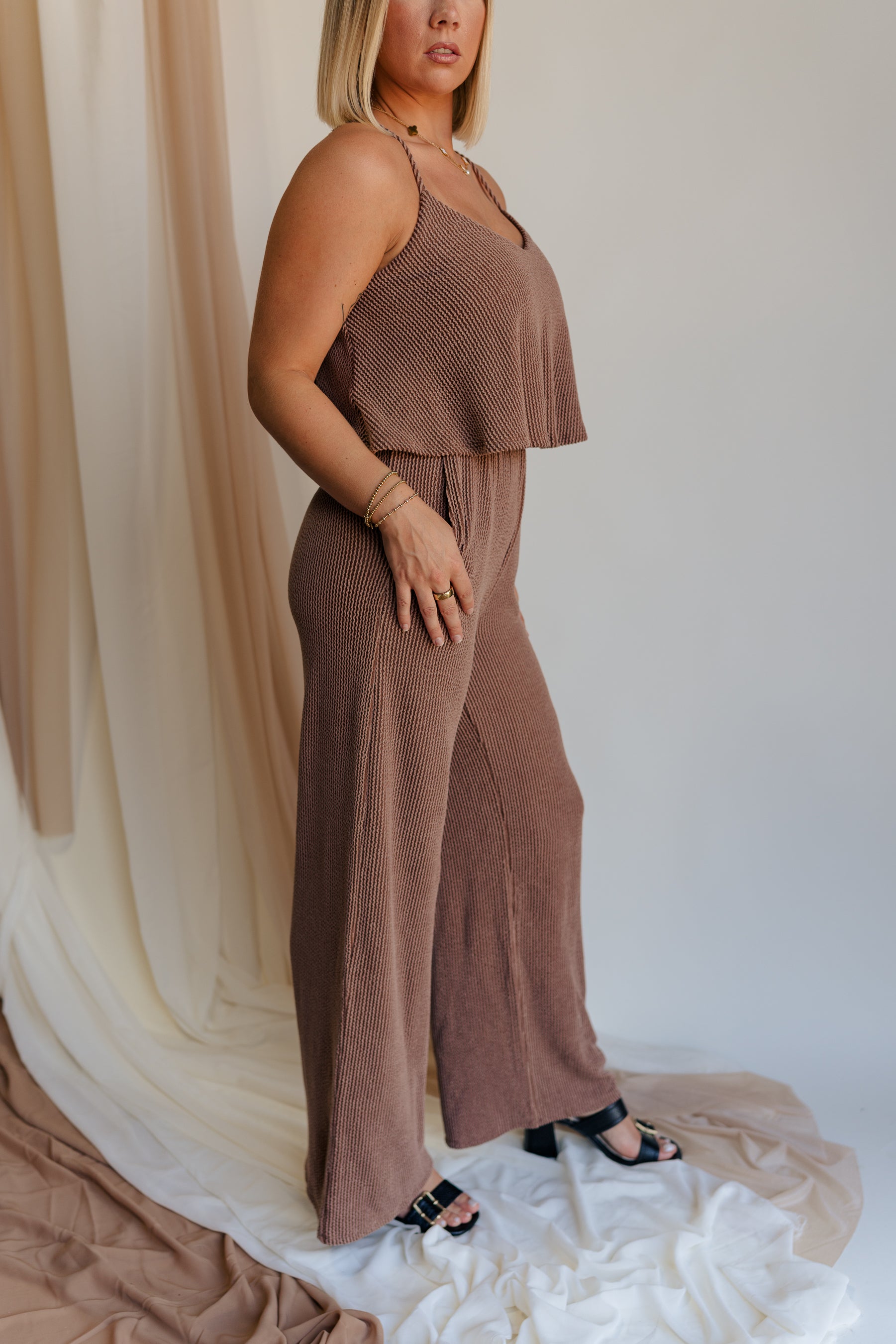 Close up side view of model wearing Kaylee Brown Ribbed Jumpsuit. This is a brown ribbed jumpsuit, with ruffle upper, and adjustable straps.