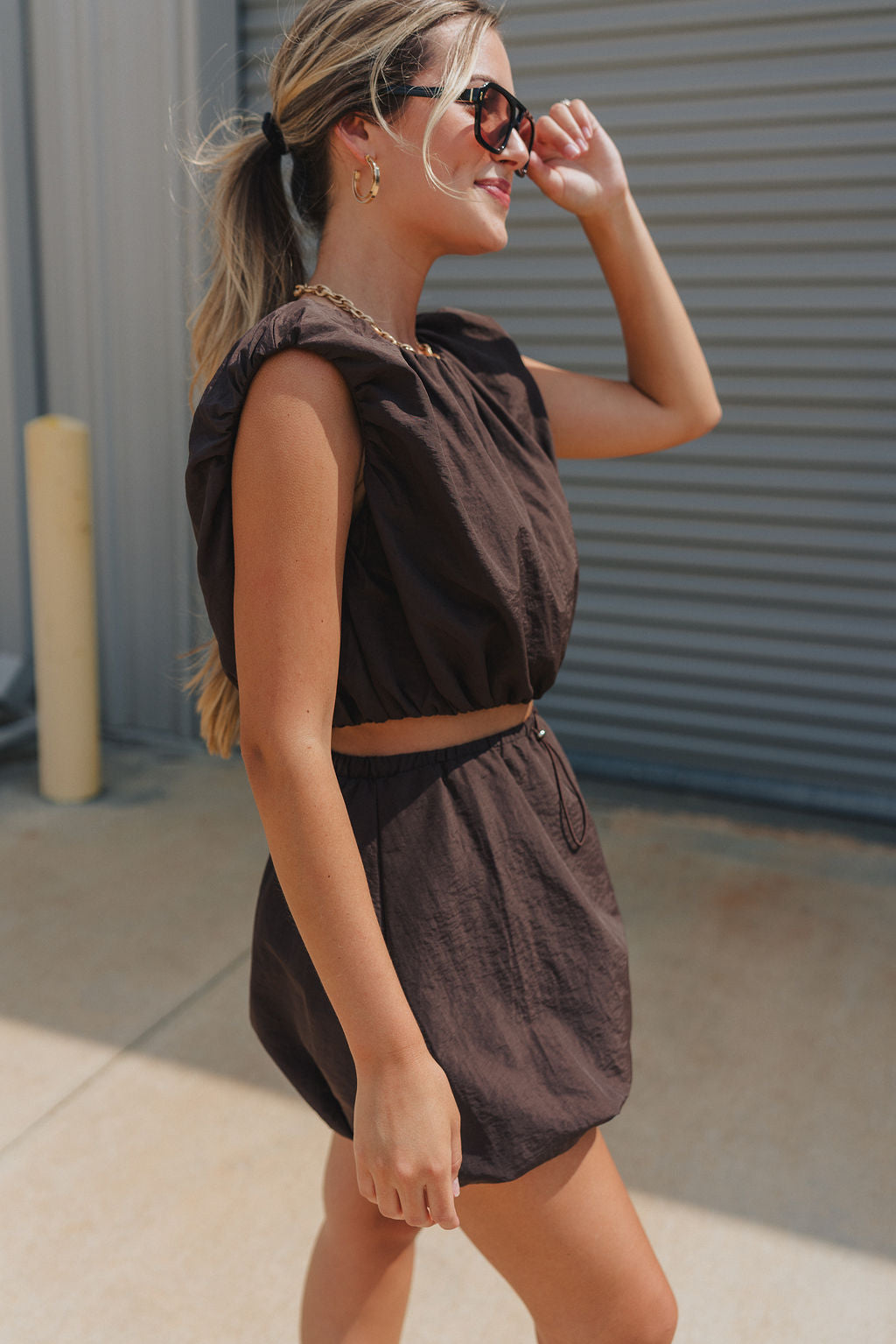 Side view of model wearing Tatum Mini Skirt in espresso. This is a mini skirt with a drawstring waistband, bubble hem, and mini length.