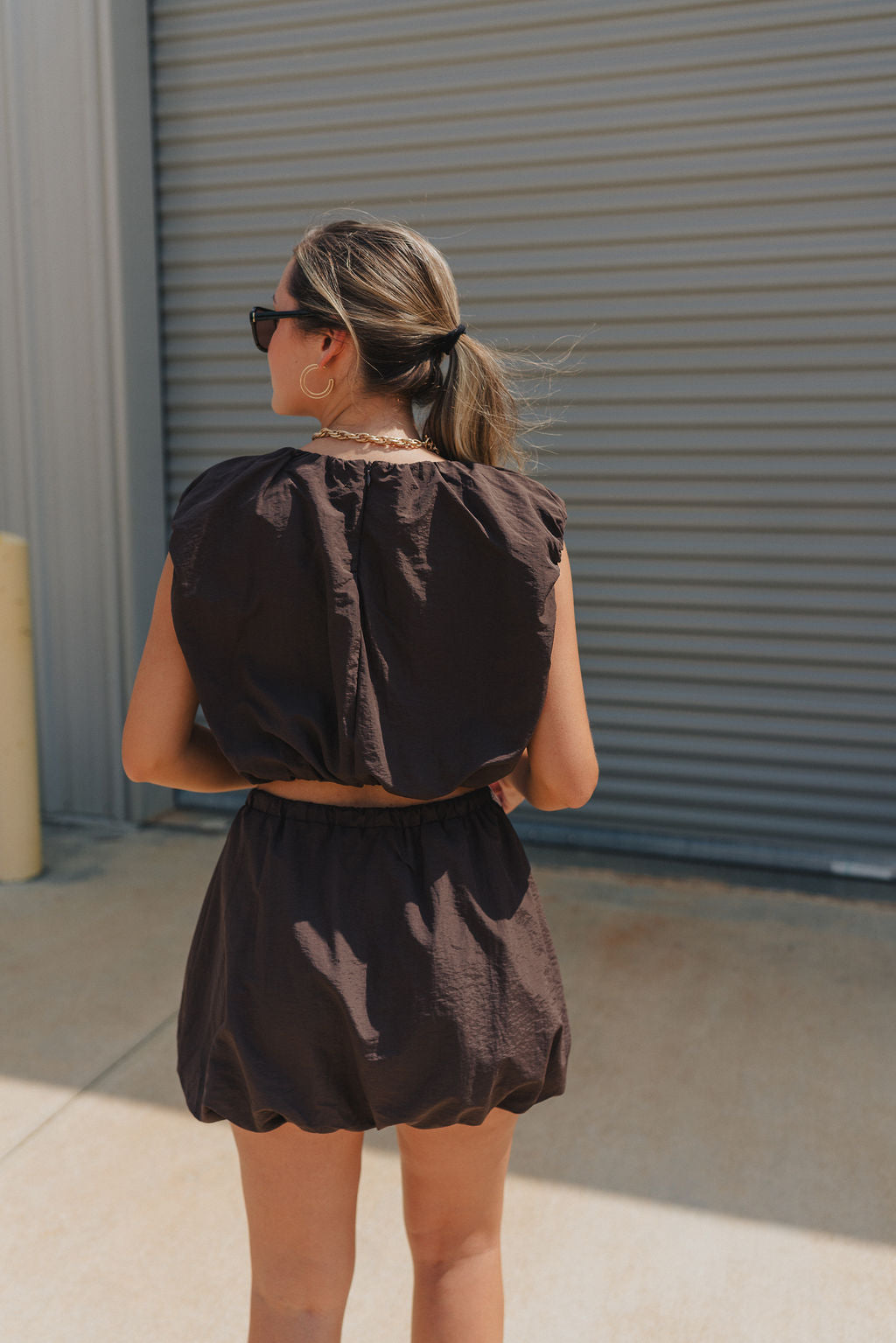Back view of model wearing Tatum Mini Skirt in espresso. This is a mini skirt with a drawstring waistband, bubble hem, and mini length.
