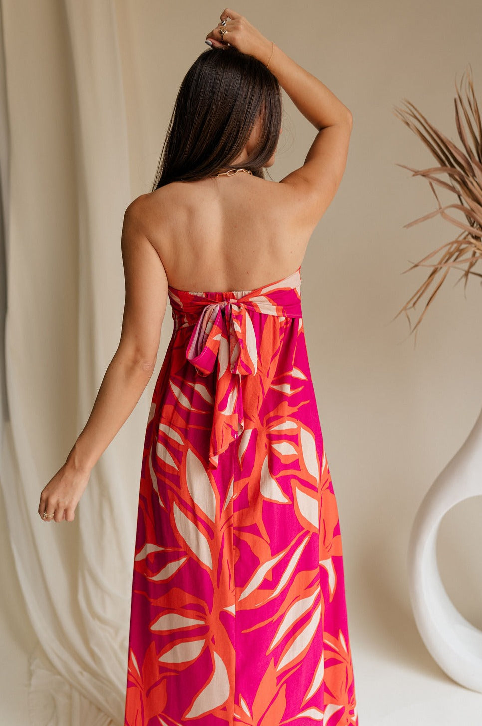 back  view of female model wearing the Luna Orange & Fuchsia Floral Maxi Dress which features Fuchsia, Red Orange and Linen Floral Print, Linen Lining, Strapless, Back Tie Detail and Maxi Length