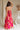 Full body back view of female model wearing the Luna Orange & Fuchsia Floral Maxi Dress which features Fuchsia, Red Orange and Linen Floral Print, Linen Lining, Strapless, Back Tie Detail and Maxi Length