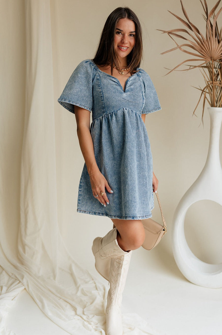 full body view of female model wearing the Charlie Light Denim V-Wire Mini Dress which features Denim Wash Fabric, Mini Length, Square Neckline with V Wire, Smocked Back and Short Puff Sleeves