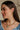 Side view of female model wearing the Vera Rhinestone & Gold Heart Shaped Huggie Earring which features heart shaped gold huggies with a clear stone detail