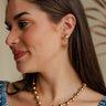 Side view of female model wearing the Vera Rhinestone & Gold Heart Shaped Huggie Earring which features heart shaped gold huggies with a clear stone detail
