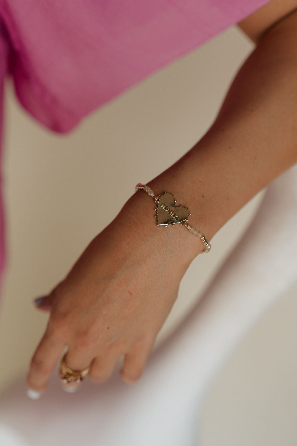 Front view of female model wearing the MAMA Ivory & Gold Beaded Adjustable Bracelet which features gold and ivory beads, heart medallion says 'MAMA" and adjustable closure.