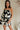front view of female model wearing the Lila Black & Cream Tie Straps Romper which features Black and White Geometric Pattern, White Shorts Lining, Two Side Pockets, Ruffle Upper, Square Neckline and Tie Straps