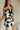 side view of female model wearing the Lila Black & Cream Tie Straps Romper which features Black and White Geometric Pattern, White Shorts Lining, Two Side Pockets, Ruffle Upper, Square Neckline and Tie Straps