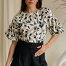 front view of female model wearing the Anaya Black & Cream Floral Puff Sleeve Top which features Cream and Black Floral Print, Cream Lining, Round Neckline, Back Key Hole with Button Closure and Short Puff Sleeves