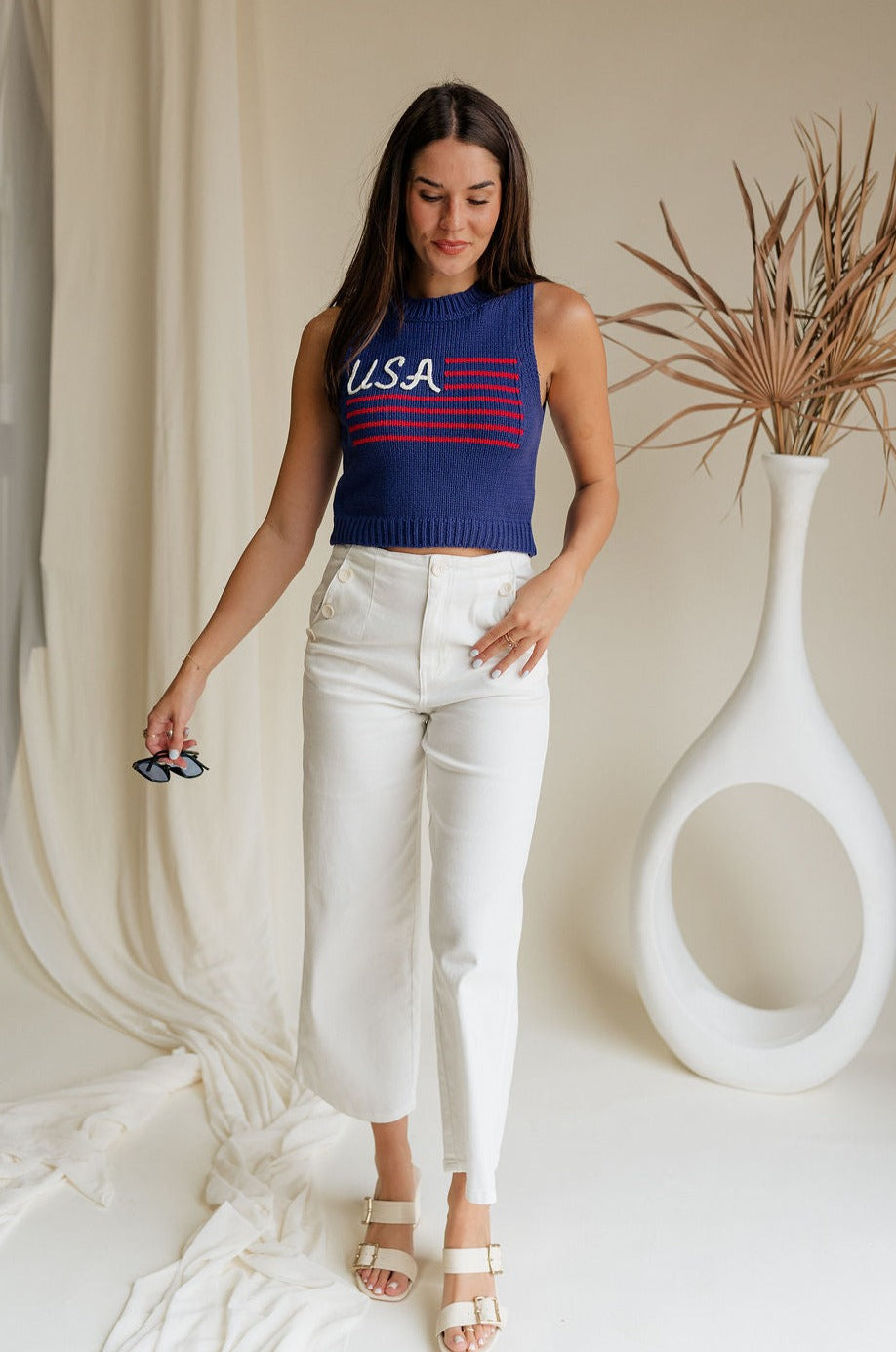 Full body front view of female model wearing the USA Navy Knit Flag Tank Top that has navy knit fabric, a stitched flag with red stripes and white USA text, and a round neck.