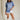 Full body front view of female model wearing the Coastal Cowgirl Light Blue Graphic Tee that has light blue fabric, a white cowgirl boot graphic, white "Coastal Cowgirl" text, short sleeves, and a round neck.