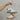 Model's hand is holding the Dolce Vita Notice Sneaker in White/Grey Leather that have white leather uppers with grey details, and a brown rubber sole.