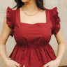 Front view of female model wearing the Adriane Burgundy Ruffle Top that has burgundy fabric, a square neck, and ruffle details.