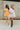 Full body view of models wearing the Tatum Orange and Cream Checkered Romper and Payton Sequin Football Mini Dress. The romper is an orange and cream checkered romper, with short sleeves, button up front, and a collared neckline. The mini dress is a white mini dress, sequin, with footballs all over and short sleeves.