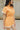 Close up side view of model wearing the Tatum Orange and Cream Checkered Romper. This is an orange and cream checkered romper, with short sleeves, button up front, and a collared neckline.