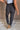 Lower body back view of female model wearing the Uma Charcoal Jogger Pants that have charcoal grey fabric, a wide elastic waistband, tapered ankles, and side & back pockets.