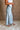 Lower body side view of female model wearing the Greer Wide Legs Jeans that have light wash denim, frayed hems, and a front zipper and button closure