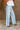 Lower body side view of female model wearing the Greer Wide Legs Jeans that have light wash denim, frayed hems, and a front zipper and button closure