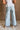 Lower body back view of female model wearing the Greer Wide Legs Jeans that have light wash denim, frayed hems, and a front zipper and button closure