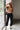 Full body front view of female model wearing the Rosalind Black Barrel Jeans with a brown tank top and black heels.