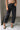 Lower body front view of female model wearing the Rosalind Black Barrel Jeans with a brown tank top and black heels.