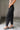 Lower body side view of female model wearing the Rosalind Black Barrel Jeans with a brown tank top and black heels.