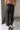 Lower body back view of female model wearing the Rosalind Black Barrel Jeans with a brown tank top and black heels.