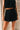 Close front view of female model wearing the Madeline Black Plisse Shorts that have black plisse fabric, elastic waist, pockets, and front tie. Worn with matching top