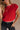Upper body front view of female model wearing the Baleigh Red Knit Top that has red knit fabric with white trim.