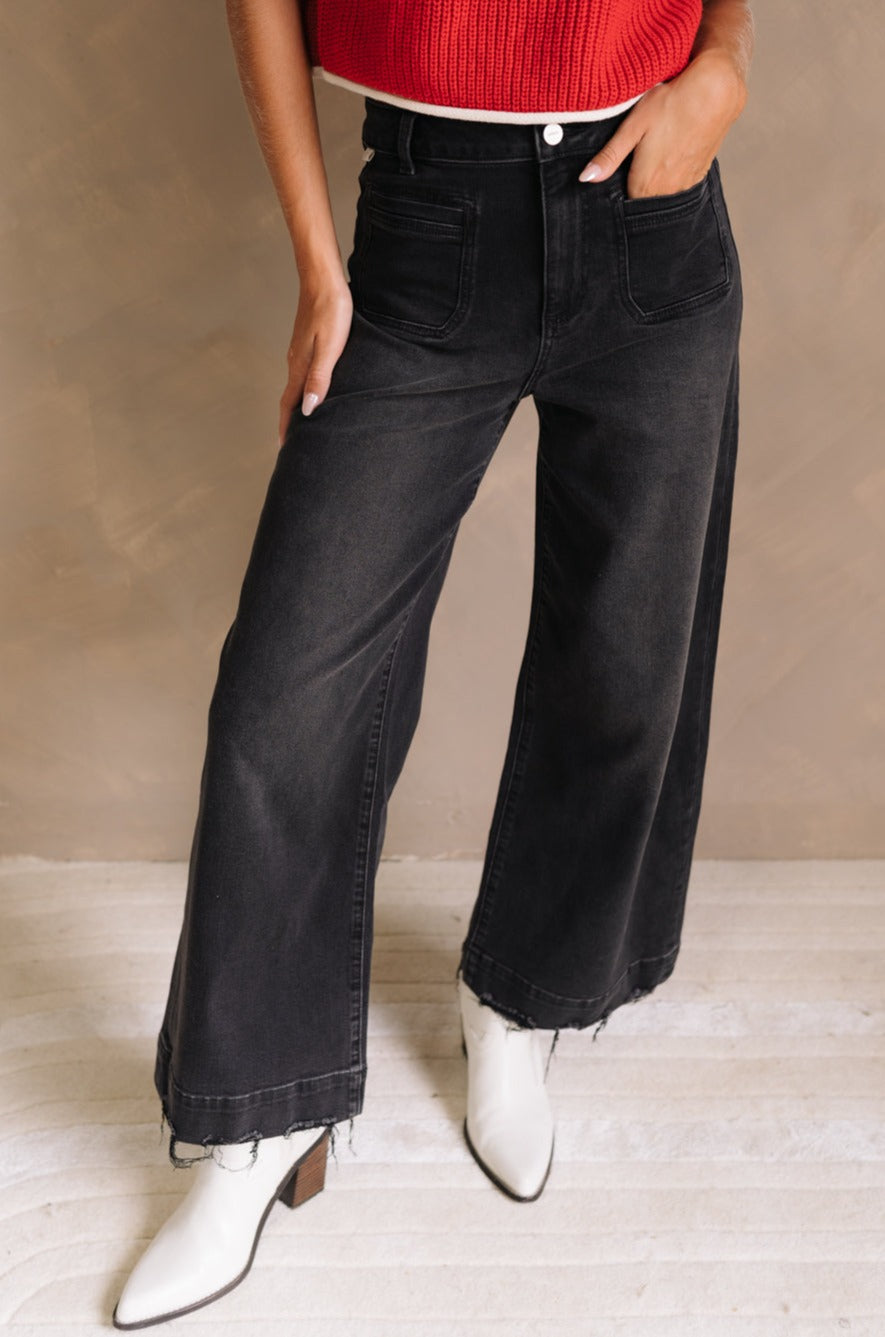 Lower body front view of female model wearing the Ceros: Florence Black Wide Leg Jeans with a red top.