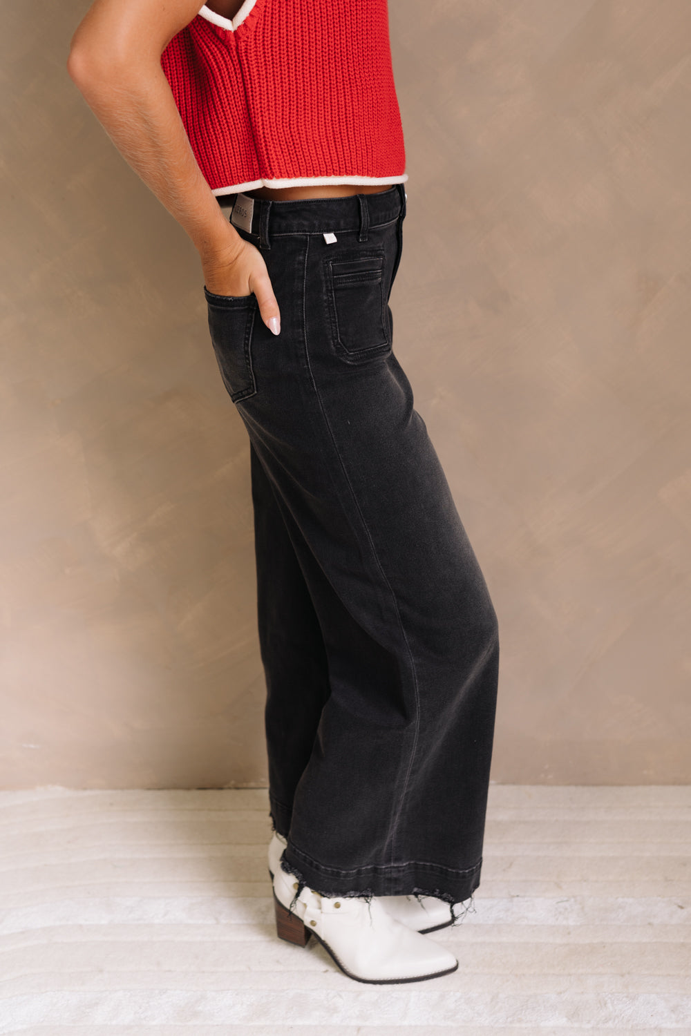 Lower body side view of female model wearing the Ceros: Florence Black Wide Leg Jeans with a red top.