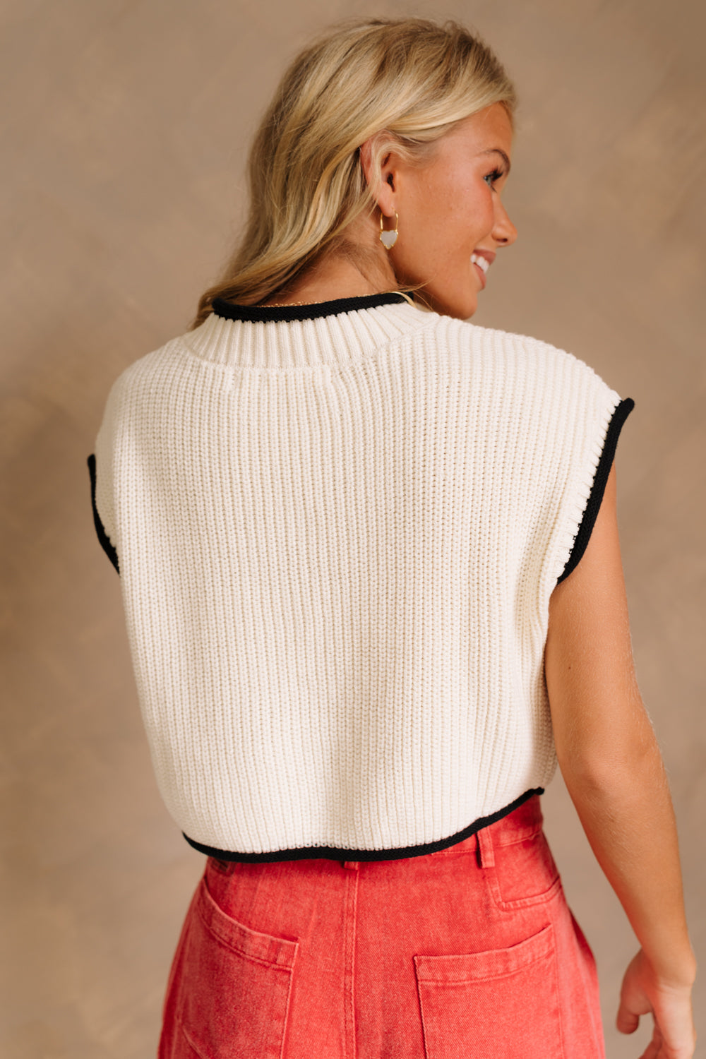 Close up of back of model wearing the Marleigh Cream Knit Top. This is a cream knit cropped top, sleeveless, with black trimming.