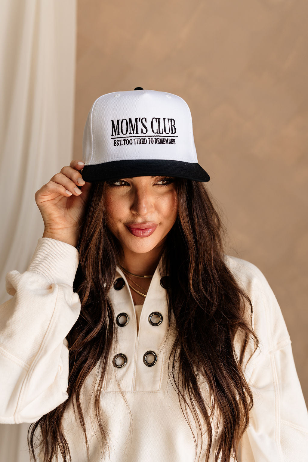 Front view of female model wearing the Mom's Club Trucker that is white with a black bill and text. Text on front says "MOM'S CLUB EST. TOO TIRED TO REMEMBER" and the back says "The happiest :)"