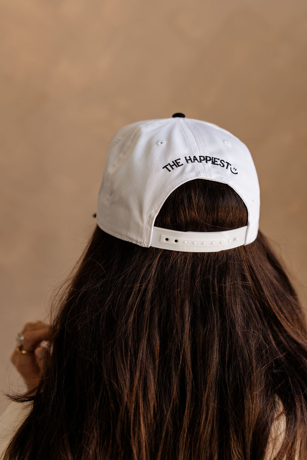 Back view of female model wearing the Mom's Club Trucker that is white with a black bill and text. Text on front says "MOM'S CLUB EST. TOO TIRED TO REMEMBER" and the back says "The happiest :)"